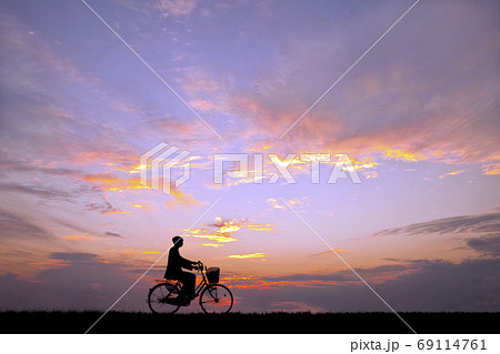 夕陽を背景に自転車通学する男子高校生のシルエットの写真素材