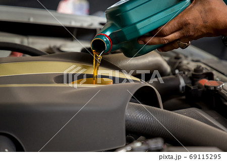 Car mechanic replacing and pouring fresh oil into engine at maintenance repair service station 69115295