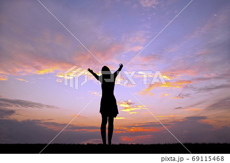 夕陽を背景にバンザイ(祈り)をする女性のシルエット 69115468