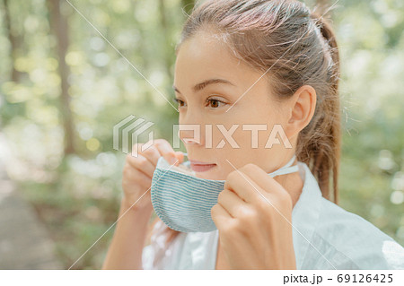 Asian beauty woman putting on mask on face. Wearing corona virus prevention masks for long hours are creating irritation, skin problems, acne pimples 69126425
