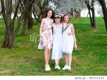 Three adorable girls in dresses hold hands in the garden, park. Three adorable girls in dresses hold hands in the garden, park. 69131432