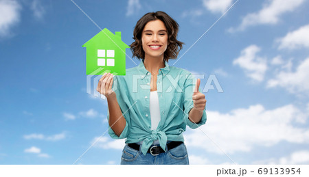 smiling woman with green house showing thumbs up 69133954