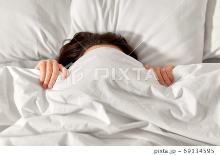 woman lying in bed under white blanket or duvet woman lying in bed under white blanket or duvet 69134595
