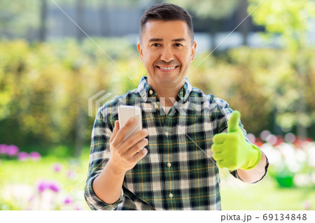 man with smartphone showing thumbs up at garden man with smartphone showing thumbs up at garden 69134848
