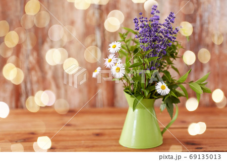 bunch of herbs and flowers in green jug on table 69135013