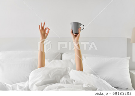 woman with cup of coffee lying in bed showing ok woman with cup of coffee lying in bed showing ok 69135202