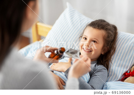 mother pouring cough syrup for sick daughter 69136000