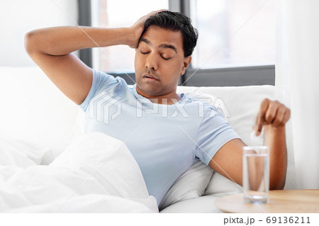 sick man in bed with medicine and glass of water sick man in bed with medicine and glass of water 69136211
