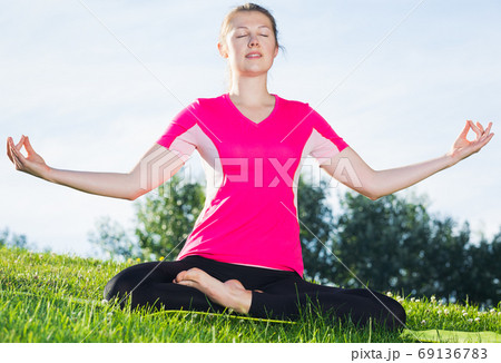 Female 26-32 years old in pink T-shirt is sitting and meditating Female 26-32 years old in pink T-shirt is sitting and meditating 69136783