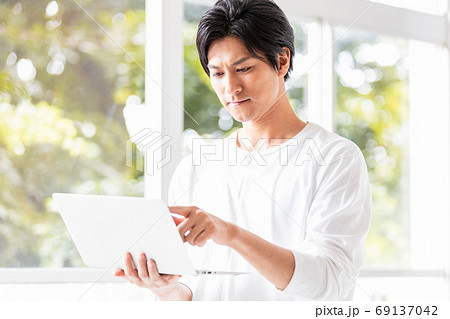 ノートパソコンを手に窓辺に立つ若い男性 ノートパソコンを手に窓辺に立つ若い男性 69137042