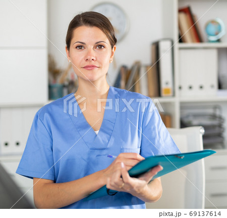 Woman doctor standing in office with clipboard in hands 69137614