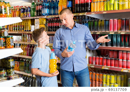 Smiling father friendly discussing with preteen boy while choosing beverages in food store Smiling father friendly discussing with preteen boy while choosing beverages in food store 69137709