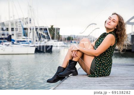 Young attractive woman tourist sitting at quay with sailboats on background Young attractive woman tourist sitting at quay with sailboats on background 69138282