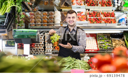 happy male seller showing assortment of grocery shop 69139478