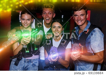 Emotional young people standing with laser guns having fun toge Emotional young people standing with laser guns having fun toge 69139664
