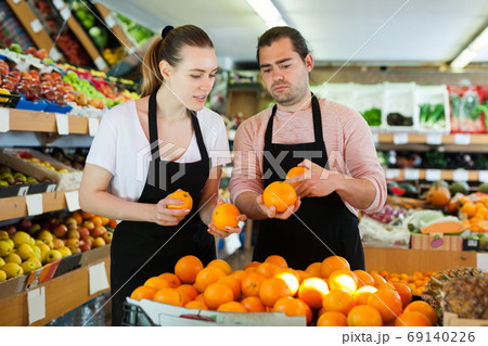 Male and woman standing and holding fresh oranges in fruit store Male and woman standing and holding fresh oranges in fruit store 69140226