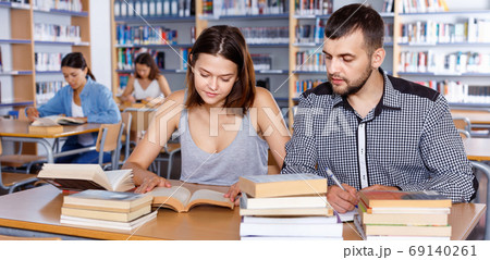 Young people reading and making notes while preparing for exam in college library Young people reading and making notes while preparing for exam in college library 69140261