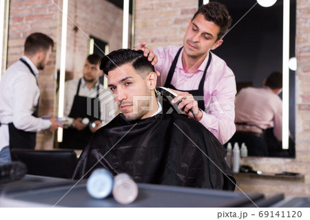 Hairdresser man doing styling of guy with electric hair clipper Hairdresser man doing styling of guy with electric hair clipper 69141120