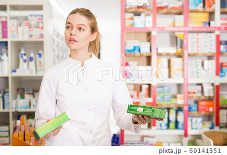 Portrait of smiling friendly female druggist in white coat working in pharmacy 69141351