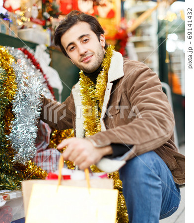Happy young man with garland looking Christmas toys at fair outdoor 69141432