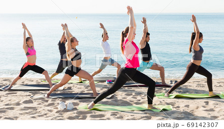 People exercising yoga poses on beach People exercising yoga poses on beach 69142307