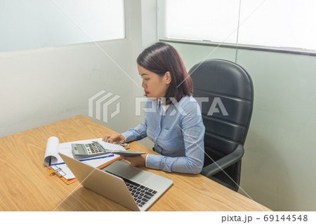 Businesswoman sitting in office room and using calculator 69144548
