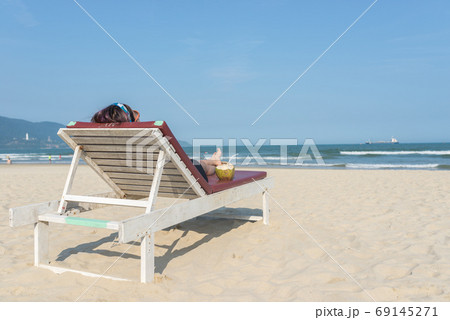 Rear view of woman lying on sandy summer beach chair  69145271