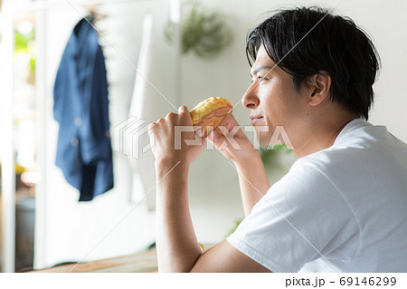 部屋でメロンパンを食べる若い男性 69146299