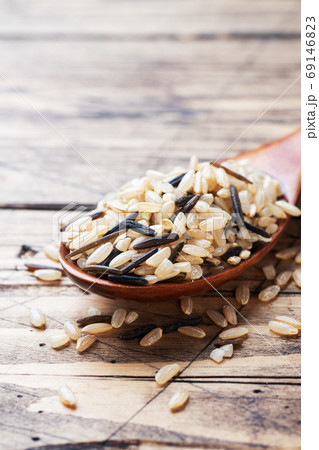 Raw wild rice in a wooden spoon. Raw rice grits on a wooden background. Copy space. 69146823