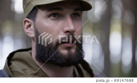 Portrait of handsome young man hunter or tourist. Man in camouflage clothes hunts outdoor in forest hunting alone. Close up of man hiker standing in forest. Hunter hunts down prey 69147688