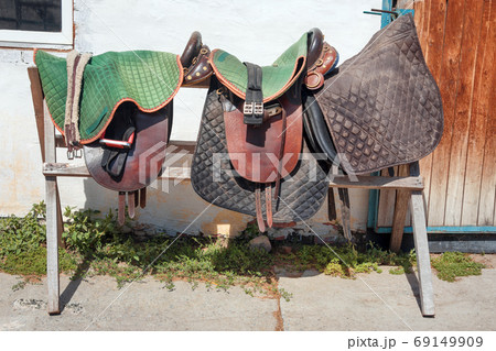 Harness for horses in horse club. Worn ranch saddles and girth. Ridding school on a horse farm Harness for horses in horse club. Worn ranch saddles and girth. Ridding school on a horse farm 69149909