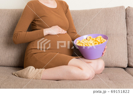 Close up of pregnant woman sitting on the sofa is eating chips because of salt cravings. Unhealthy junk food during pregnancy concept Close up of pregnant woman sitting on the sofa is eating chips because of salt cravings. Unhealthy junk food during pregnancy concept 69151822