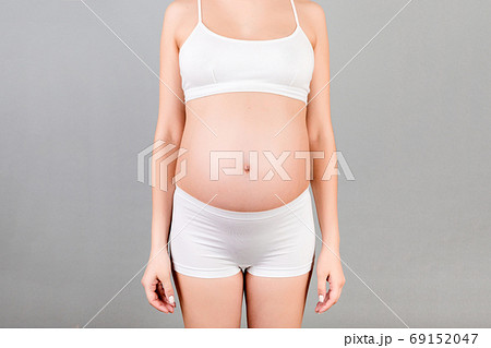 Cropped shot of pregnant abdomen in white underwear at gray background. Young woman is waiting for a baby. Copy space Cropped shot of pregnant abdomen in white underwear at gray background. Young woman is waiting for a baby. Copy space 69152047