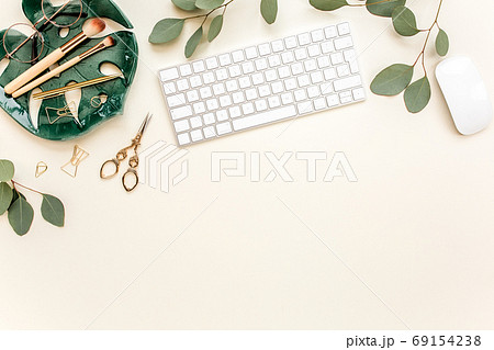Flat lay home office desk. Female workspace with computer, plate sheet monstera, golden accessories, eucalyptus leaves, on beige background. Top view 69154238