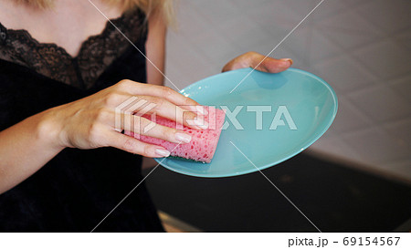 Blue plate with pink dish sponge in hand on blurred background Blue plate with pink dish sponge in hand on blurred background 69154567