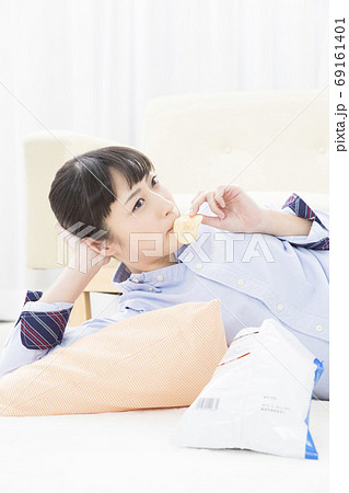 寝転んでポテトチップスを食べる女の子の写真素材 69161401 Pixta
