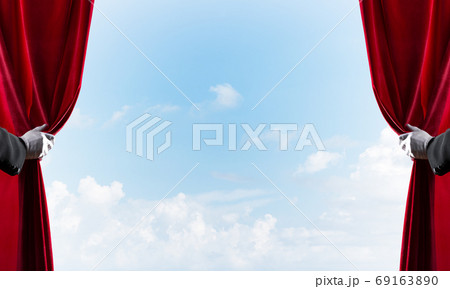 Cloudy landscape behind red curtain and hand holding it 69163890