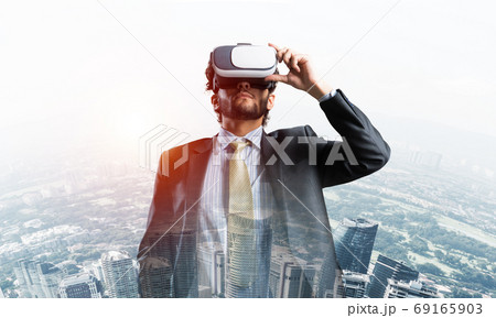 Handsome elegant businessman experiencing impressive virtual reality and business city at backdrop 69165903