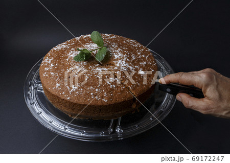 Woman cutting a chocolate cake with sugar decoration with a knife Woman cutting a chocolate cake with sugar decoration with a knife 69172247