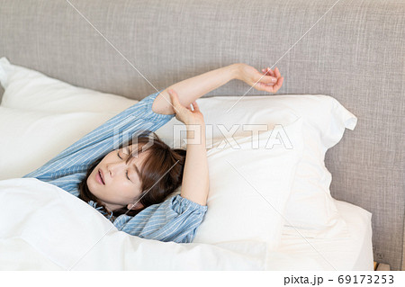 朝ベッドの中からなかなか起きられない若い女性の写真素材