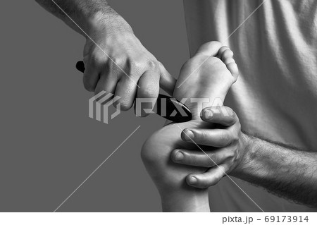 Male masseur hands doing massage on female foot reflex zone in the spa salon using gua sha scraping acupuncture tool. Male masseur hands doing massage on female foot reflex zone in the spa salon using gua sha scraping acupuncture tool. 69173914