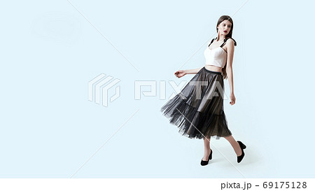 Young beautiful brunette girl in waving dark box pleated midi skirt posing in studio. Woman dancing or making a step. 69175128