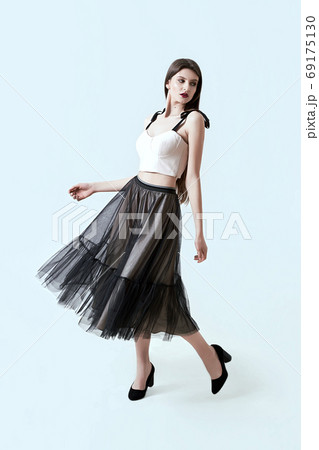 Young beautiful brunette girl in waving dark box pleated midi skirt posing in studio. Woman dancing or making a step. 69175130