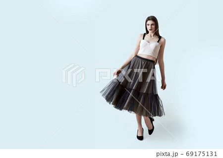 Young beautiful brunette girl in waving dark box pleated midi skirt posing in studio. Woman dancing or making a step. 69175131