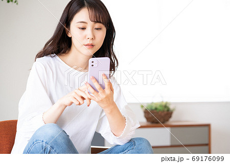 リビングでスマホを持って椅子に座る不安顔の若い女性 69176099