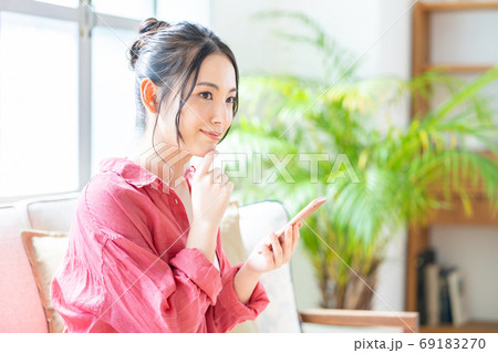 ソファでくつろぎながらスマホを操作する女性。 ソファでくつろぎながらスマホを操作する女性。 69183270
