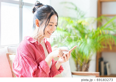 ソファでくつろぎながらスマホを操作する女性。 69183273