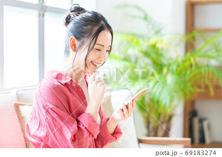 ソファでくつろぎながらスマホを操作する女性。 ソファでくつろぎながらスマホを操作する女性。 69183274
