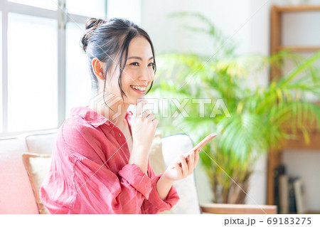 ソファでくつろぎながらスマホを操作する女性。 69183275
