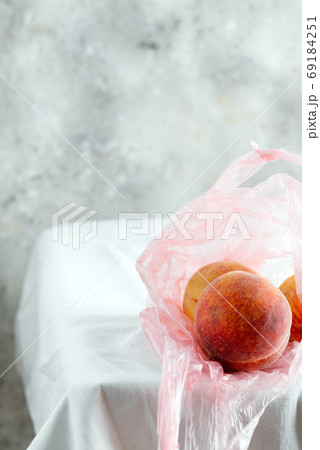 Plastic bag with natural fresh organic peach fruits on a tablecloth against grey wall background. 69184251